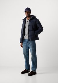Navy puffer jacket with a hood, gray polo shirt, blue jeans, and brown shoes. The jacket features a zip closure and ribbed cuffs.