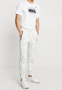 Vit Nike T-shirt med svart logotyp, matchad med ljusgrå camouflagedressbyxor med sidfickor och kontrasterande svarta ränder. Vita sneakers.