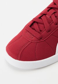Røde semskede sneakers med hvid gummisål. Har sytede detaljer og teksturerede snørebånd, der viser et enkelt, sporty design.