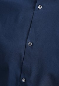 Granatowa koszula na guziki wykonana z gładkiej tkaniny, z ostro zakończonym kołnierzykiem, przednią listwą zapinaną na pięć metalowych guzików oraz eleganckim, dopasowanym krojem.