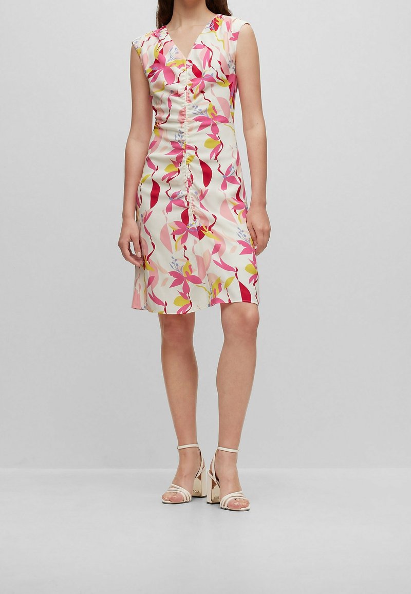 Robe à motif floral avec un décolleté en V, des manches courtes et un devant froncé, dans des couleurs pastel rose, jaune et vert.
