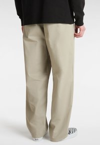 Pantalon en coton beige avec une coupe droite, doté de poches latérales et d'une texture lisse, associé à des chaussures à enfiler à motifs.