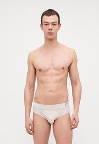 Beige Unterwäsche aus weichem Material, ausgestattet mit einem breiten elastischen Bund mit Branding, designed für eine bequeme Passform und einem klassischen Unterhosen-Schnitt.