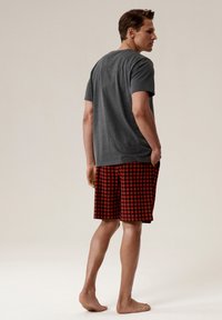 Szary t-shirt z krótkim rękawem i czerwone szorty w kratę, z mieszanki bawełny, o luźnym kroju. Model stoi boso, z rękami w kieszeniach.