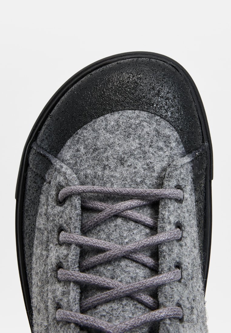Grijze felt schoen met zwarte rubberen accenten. Heeft ronde veters in een gevlochten textuur en een ronde neus, die een stevige ontwerpelement benadrukken.