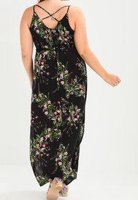 Mustavalkoinen kukallinen maksimekko, jossa on vaaleanpunaisia ja vihreitä kasviaihioita, spagettiolkaimet ja ristikkäinen selkädesign sekä virtaava siluetti.