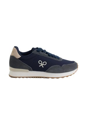 Zapatilla deportiva azul marino y gris con suela blanca, cordones azul marino, parche beige en el talón y logotipo blanco de raquetas cruzadas en el lateral.