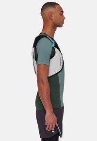 Hydration vest in black and white with adjustable straps, featuring a tube for water access, worn over a teal and green athletic shirt.