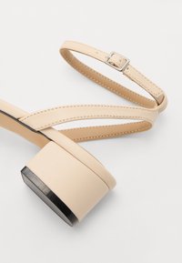 Sandales à plateforme beiges avec un talon épais texturé, une fine bride de cheville avec boucle et un design à bandes croisées sur la semelle.
