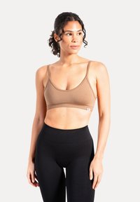 Brązowy bezszwowy biustonosz bralette z cienkimi ramiączkami i zaokrąglonym dekoltem, w połączeniu z czarnymi legginsami z wysokim stanem. Gładka tekstura, bez ozdób.