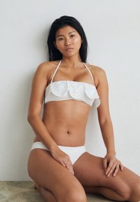 Bela bikinijeva postava s šalom, vezenim na oči, bandeau vrhom in ujemajočimi se hlačkami. Gladek material z oprijetim krojem.