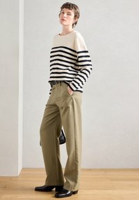 Ριγέ μακρυμάνικο τοπ σε κρεμ και ναυτικό μπλε, συνδυασμένο με ελαιόχρωμα παντελόνια φαρδιάς γραμμής, συμπληρωμένο από μαύρες μπότες μέχρι τον αστράγαλο και μια μαύρη τσάντα.