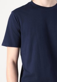 Camiseta de algodón azul marino con mangas cortas, cuello redondo y textura suave; presenta un corte estándar y sin patrones visibles.