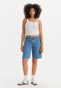 Lys blå denimshorts med avslappet passform, kombinert med en hvit ribbestrikket tanktopp og hvite sokker med svarte striper og sneakers.