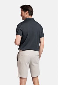 Donkergrijze polo met korte mouwen, gecombineerd met lichtbeige shorts met twee achterzakken en een schone, eenvoudige uitstraling.
