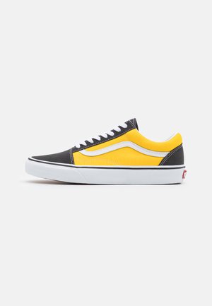 Svart og gul kanvas sneakers med en hvit stripe, med gummisåle og hvite snører. Klassisk lavtopp-silhuett, kontrasterende farger.