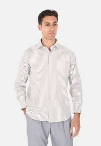 Camicia bianca a maniche lunghe con sottili righe verticali marroni, colletto button-down e una tasca sul petto. Il tessuto appare liscio e leggero.