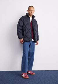 Černá prošívaná bunda s diamantovým vzorem, nošená přes bordový svetr, modré džíny a růžové tenisky s bílými pruhy.