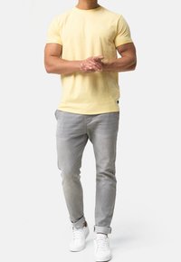 Yellow cotton t-shirt with short sleeves, paired with light gray slim-fit pants. White sneakers complete the outfit. Simple design, no patterns.