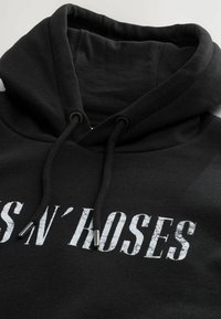 Felpa nera realizzata in morbido tessuto, caratterizzata da una grande stampa bianca distressata con la scritta "GUNS N' ROSES", cordini regolabili e punte in metallo.