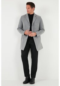 Abrigo gris de mezcla de lana con cuello con muesca, cierre de un solo botón y bolsillo delantero, llevado sobre un suéter de cuello alto negro y pantalones negros.