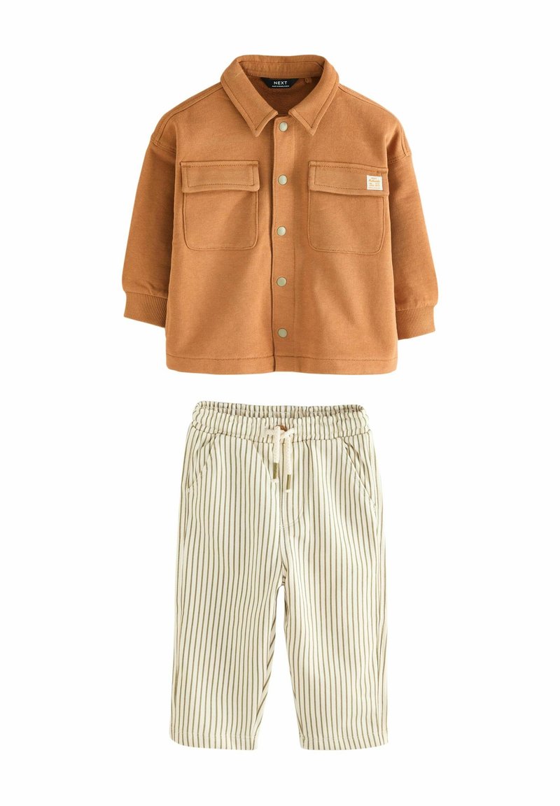 Veste marron boutonnée avec deux poches avant, associée à un pantalon crème à taille élastique présentant de fines rayures verticales marron.