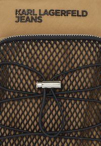 Schwarzer Netzstoff mit einem Reißverschluss, versehen mit dem eingeprägten Schriftzug "KARL LAGERFELD JEANS" in Schwarz. Enthält einen silbernen Hardware-Akzent und elastische Details.