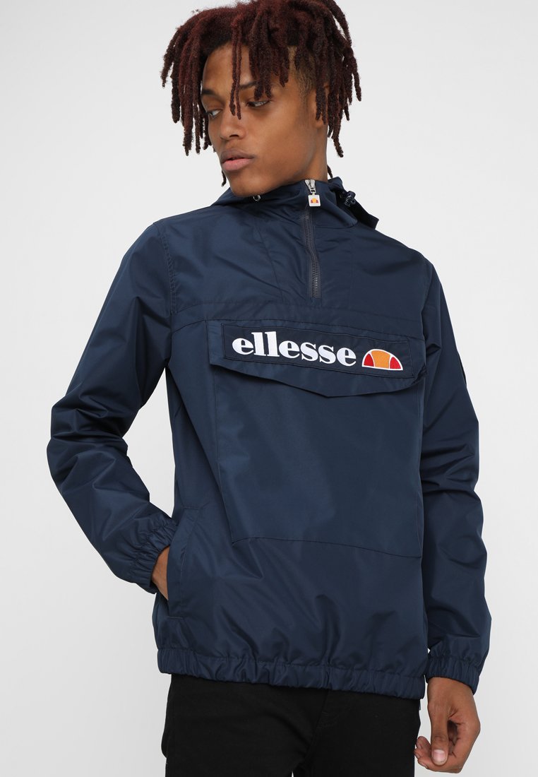 Corta-vento azul-marinho com gola alta, punhos e barra elásticos, apresentando um grande bolso frontal e o logotipo branco "ellesse" no peito.