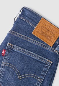 Μπλε τζιν παντελόνι Levi's διπλωμένο, με έμφαση στην πίσω τσέπη με ραφές, κόκκινη ετικέτα Levi's και καφέ δερμάτινο ταμπελάκι της μάρκας στη ζώνη μέσης.