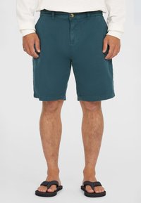 Pantaloni corti color teal realizzati in un tessuto leggero con una superficie liscia, dotati di chiusura con bottone, passanti per la cintura e design alla lunghezza del ginocchio.