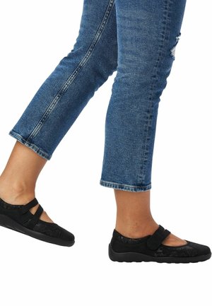 Zapatos negros estilo Mary Jane con dos tiras de Velcro, con una parte superior de textil estampado y una suela de goma texturizada. Combinados con jeans azules recortados.