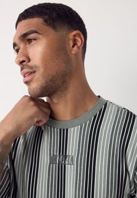 Gestreiftes Kurzarmhemd in Grau und Schwarz mit strukturierter Stoffqualität, ausgestattet mit Rundhalsausschnitt und gesticktem Logodetail auf der Vorderseite.