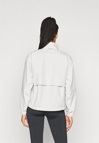 Casaco corta-vento branco com gola alta, mangas franzidas e um design de costas cropped. Textura suave com detalhes mínimos.