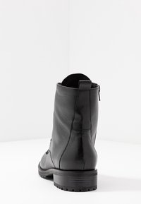 Bottine en cuir noir avec un talon carré, texture lisse, fermeture éclair sur le côté et design minimaliste.