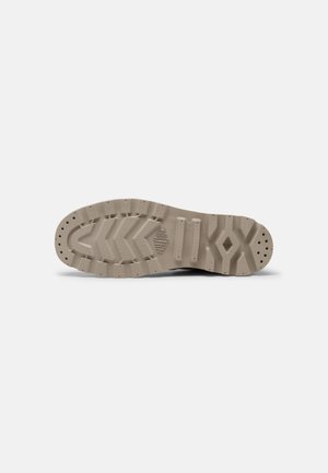 Sneaker outsole in beige rubber with a textured traction pattern, featuring grooves and rounded edges for grip and stability.