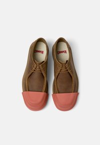Brown leather shoes with a rubber orange toe cap, featuring a rounded design, laces, and a beige insole marked with "CAMPER."