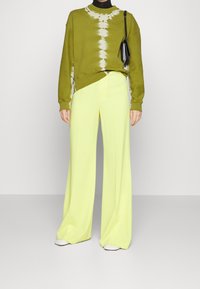 Zielony sweter z wzorem tie-dye z bawełny, połączony z szerokimi neonowymi żółtymi spodniami i białym obuwiem. Posiada luźny krój i kontrastujące faktury.