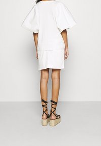 Top blanco con mangas abullonadas combinado con una falda blanca, complementado con sandalias de cuña negras con tiras y plataforma de tejido.