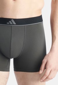 Boxerky v tmavě zelené látce s černým elastickým pasem ozdobeným šedými logy a kontrastním prošitím. Přiléhavý střih.