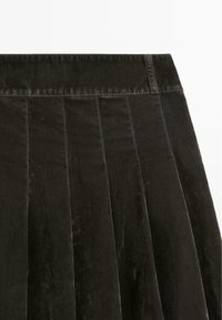 Black corduroy skirt featuring a pleated design, a flat waistband, and visible stitching patterns, showcasing a soft, textured finish.