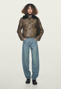 Brown leather jacket with a black fur collar, paired with loose blue denim jeans and black ankle boots. Textured fabric details are visible.