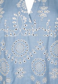 Blouse bleu clair avec des motifs floraux et circulaires brodés en blanc, détails découpés, design en v et texture douce.