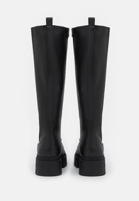 Bottes noires montant jusqu'aux genoux en matériau synthétique lisse. Elles disposent d'une semelle épaisse et de deux languettes en haut pour un enfilage facile.