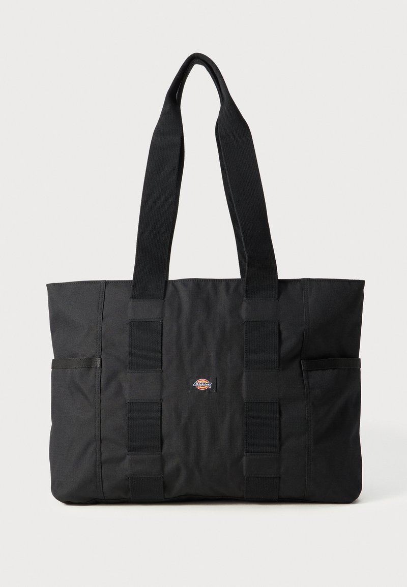 Svart tote bag med doble håndtak, laget av slitesterkt stoff. Har to sidelommer og en liten logo i midten. Enkel, rektangulær design.