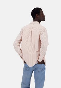 Camicia a maniche lunghe a righe rosa chiaro e bianco, con collo a bottoni, orlo curvo, cuciture visibili e dettaglio con piega sul retro.