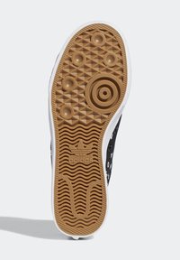 Svart sneakersula med en texturerad brun gummiyttersula, prydd med runda knoppar och spår för grepp, samt en vit mellansula.