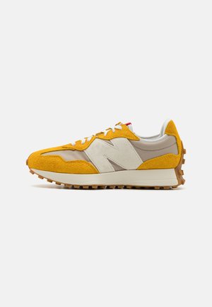 New Balance Sneaker mit einem Obermaterial aus senfgelbem Wildleder, weißen und beigen Akzenten sowie einer braunen strukturierten Gummisohle.