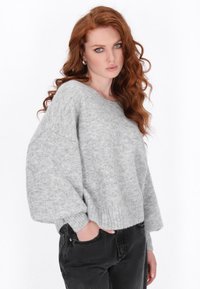 Helle graue Strickjacke mit lockerer Passform, geripptem Saum und weiten Ärmeln. Kombiniert mit schwarzen hochgeschnittenen Jeans.