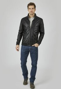 Chaqueta de cuero negra con zipper frontal, puños y collar acanalados; combinada con jeans azules y botas marrones. Textura suave, diseño ajustado.