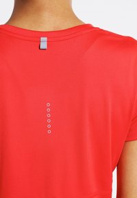 Camiseta deportiva roja con cuello redondo y una serie de pequeños puntos grises en la espalda, confeccionada con tejido suave que absorbe la humedad.
